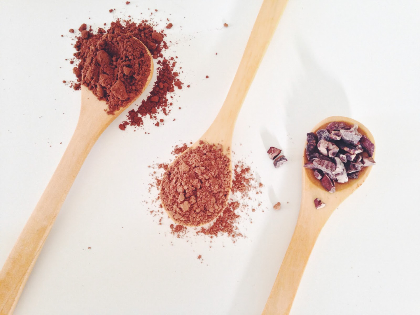 Three wooden spoons with cocoa powder, cacao powder, and cacao nibs