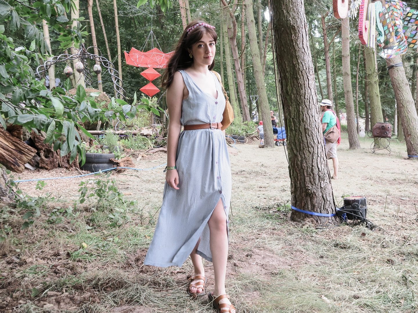 Besma stands in a forest in a blue dress with brown belt