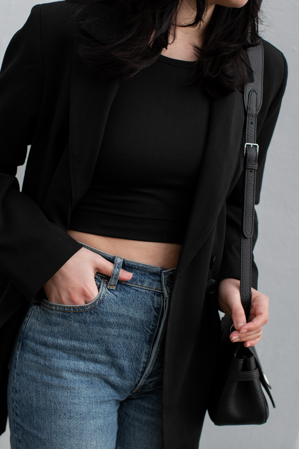 Close-up of Besma wearing Organic Basics black crop top with blue jeans and black blazer
