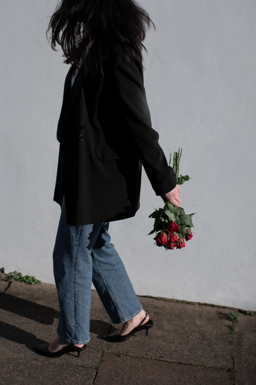 Back of woman wearing blazer and jeans holding roses