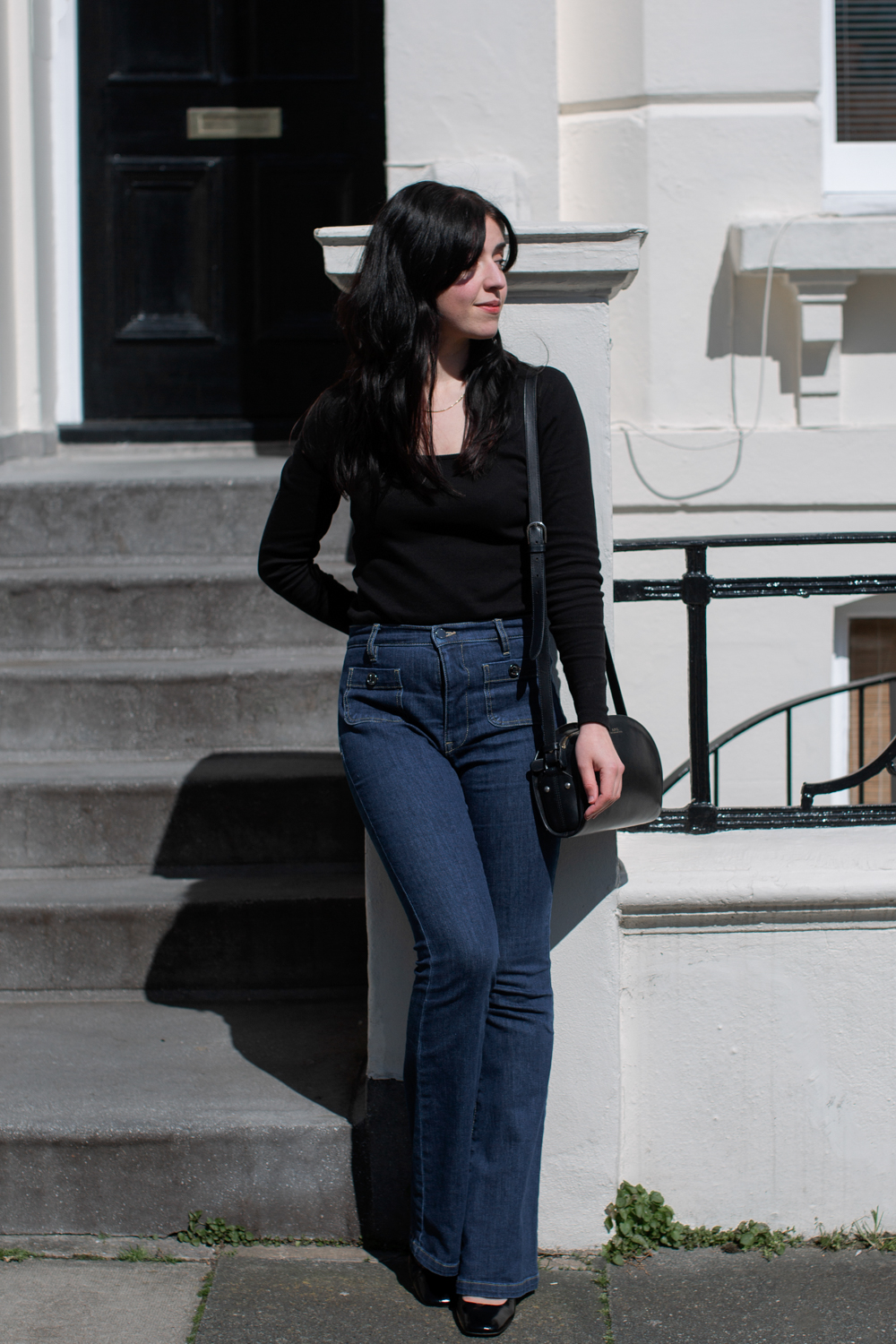 Besma leans against wall wearing black top and jeans