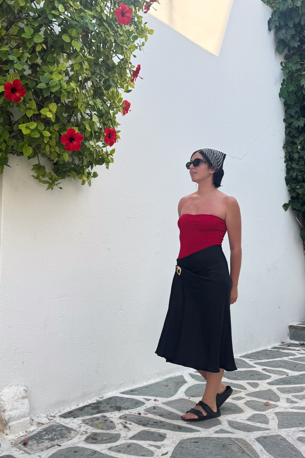 Besma wearing red next to red flowers in the Cyclades