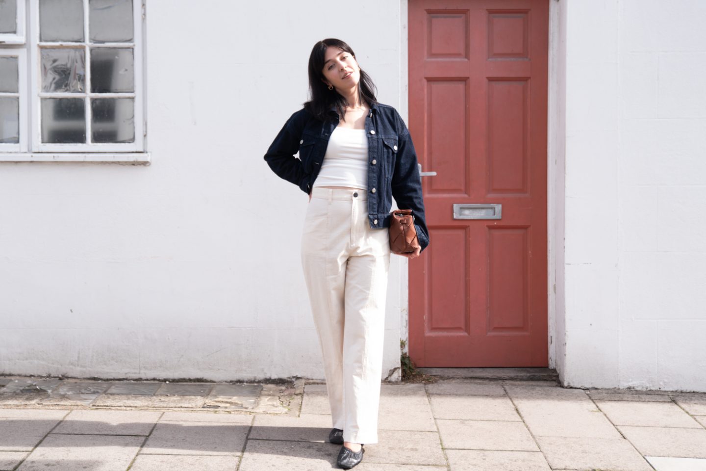 Besma wears outfit made from sustainable fabrics: denim jacket, organic cotton top, linen trousers, upcycled leather bag